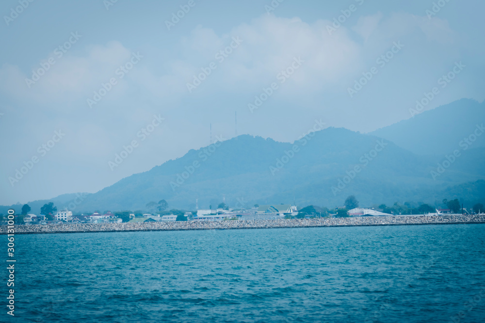 A picture of a land of sea with a background of communities and mountains.