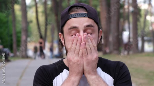 Man portrait at park street. Tired male cover his face by hands and cannot concentrate. Addicted man concept. photo