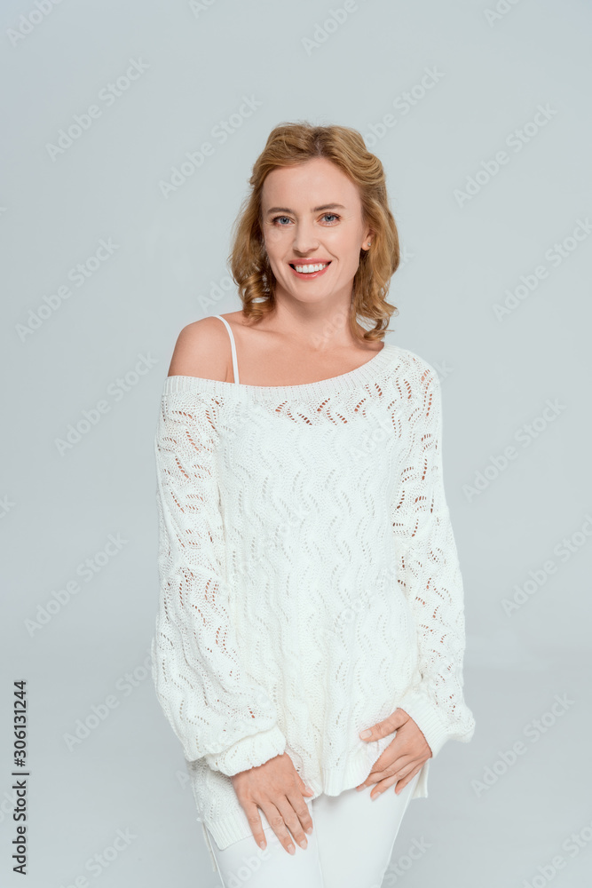 attractive and smiling woman looking at camera isolated on grey