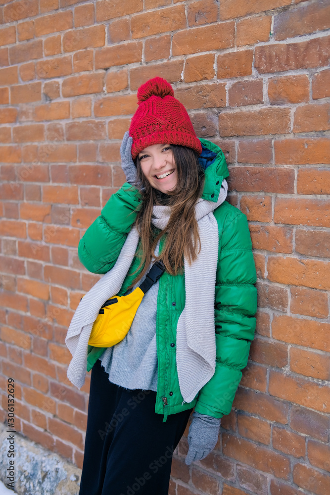 Woman hipster in bright clothes laughing and smiling. Young happy girl in a red knit hat, green jacket, grey scarf, yellow small bag. Women's fashion. Woman hipster in bright clothes laughing and smiling. Young happy girl in a red knit hat, green jacket, grey scarf, yellow small bag. Women's fashion.