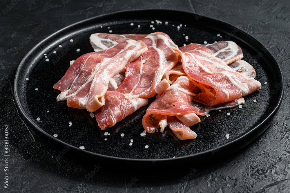 Pork bacon on a black plate. Farm organic meat. Black background. Top view