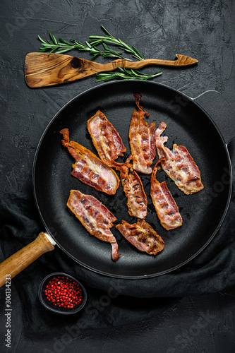 Cooked sizzling hot tasty crispy bacon on a skillet. Farm organic meat. Black background. Top view