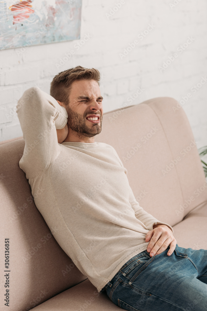 young man sitting on sofa and suffering from pain in neck