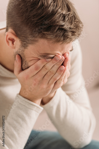 young man covering face with hands while suffering from migraine