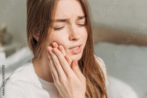 young woman touching cheek while suffering from toothache