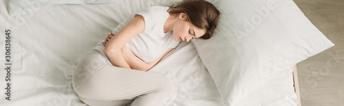Εκτύπωση καμβά top view of young woman lying in bed and suffering from stomach pain, panoramic