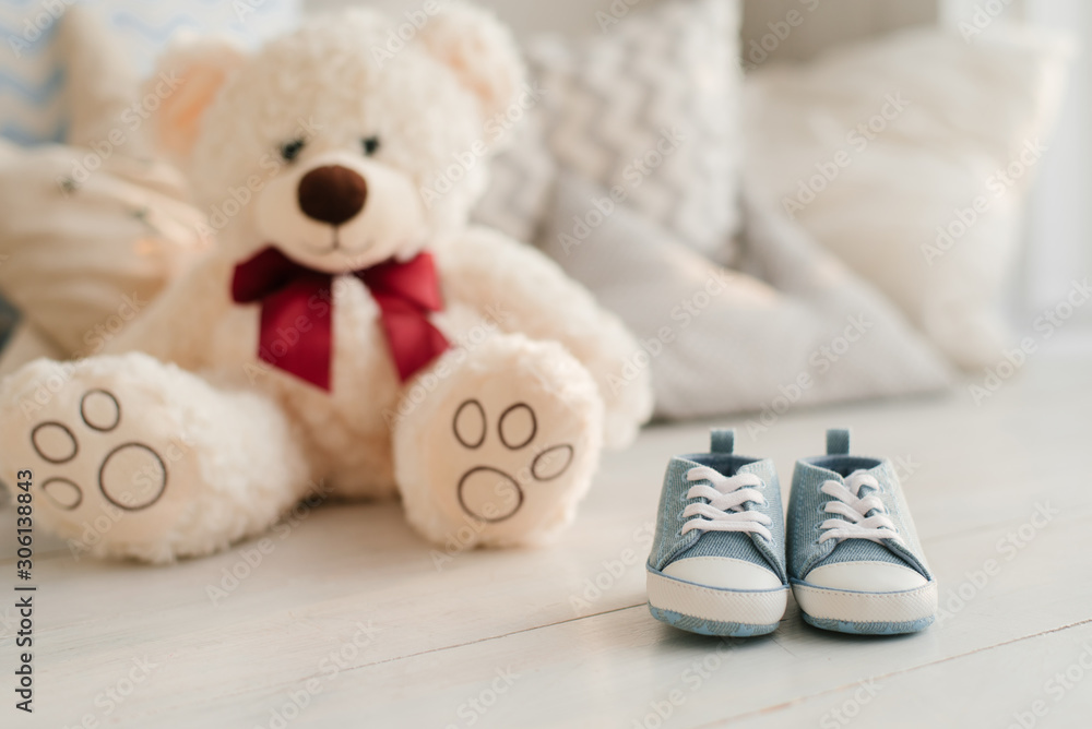 Small children's blue sneakers lie on the table against the background of pillows and soft toys . The concept of waiting for a newborn.