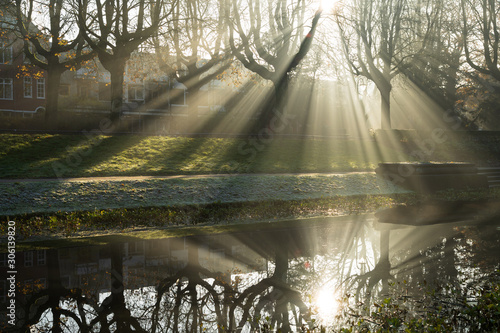 Fototapeta Naklejka Na Ścianę i Meble -  Sunbeams shining through the tree's on a foggy, autumn morning reflected in a pond.