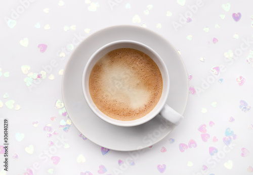 Holographic glitter confetti in heart shape and cup of coffee on white background
