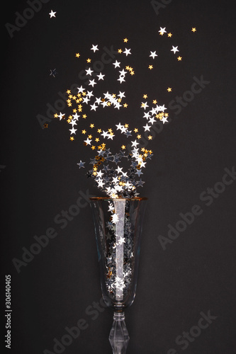 Gold and silver spangles pour from a crystal champagne glass. The concept of the Christmas and holiday season