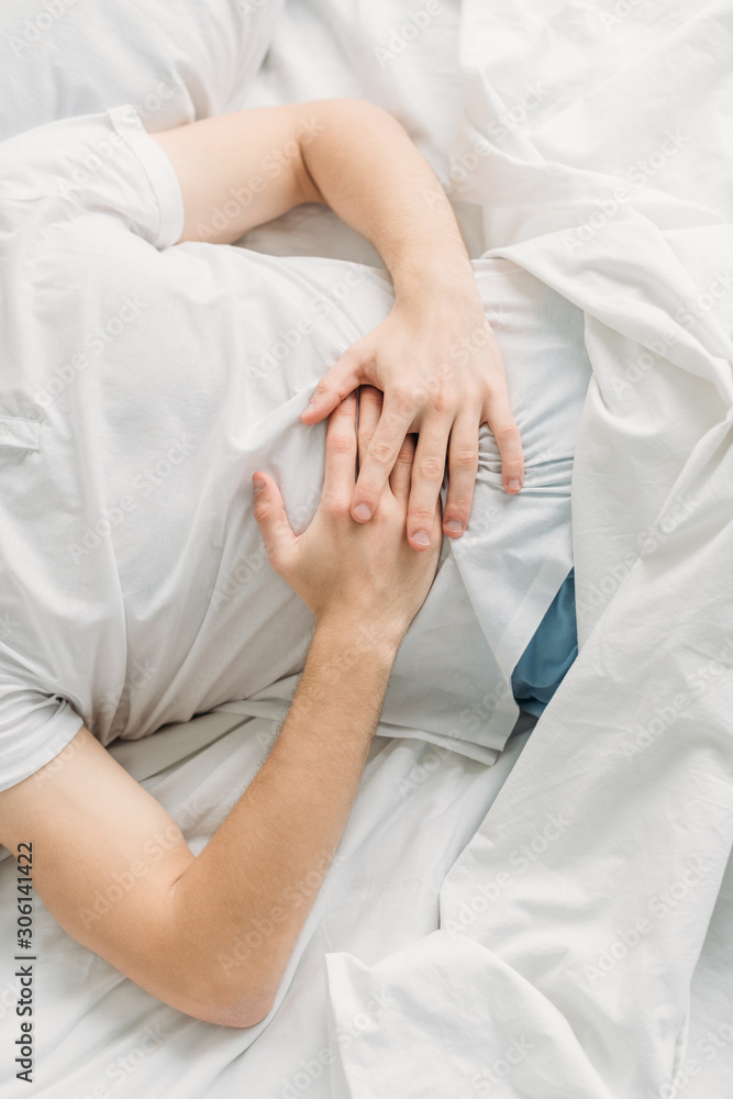 cropped view of man lying on white bedding and suffering from abdominal pain cropped view of man lying on white bedding and suffering from abdominal pain