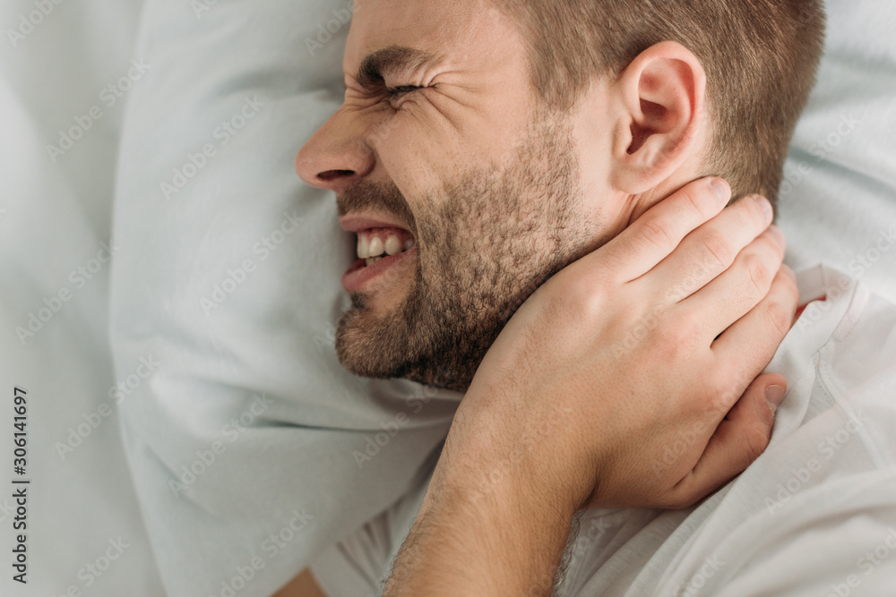 Fototapeta premium top view of young man touching neck while suffering from pain