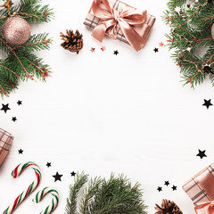 Golden baubles, gifts wrapped in craft paper, pine branches, confetti on white wood. Christmas flat lay with decorations and presents on white wooden background, copy space, top view.