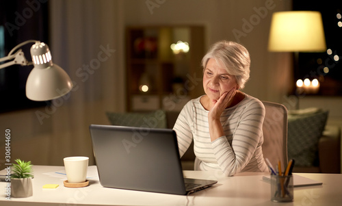 technology, old age and people concept - senior woman with laptop at home in evening