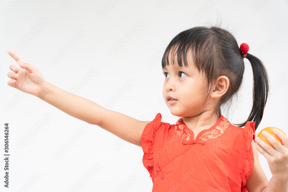 Adorable asian little girl with beautiful eyes in the red chinese dress is holding the orange and she is pointing on the right and smiling with fully happiness moment. Adorable asian little girl with beautiful eyes in the red chinese dress is holding the orange and she is pointing on the right and smiling with fully happiness moment.