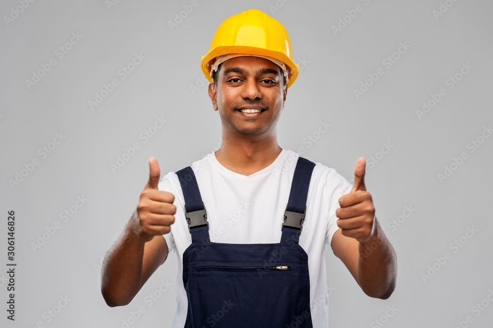 profession, construction and building - happy smiling indian worker or builder in helmet showing thumbs up over grey background profession, construction and building - happy smiling indian worker or builder in helmet showing thumbs up over grey background
