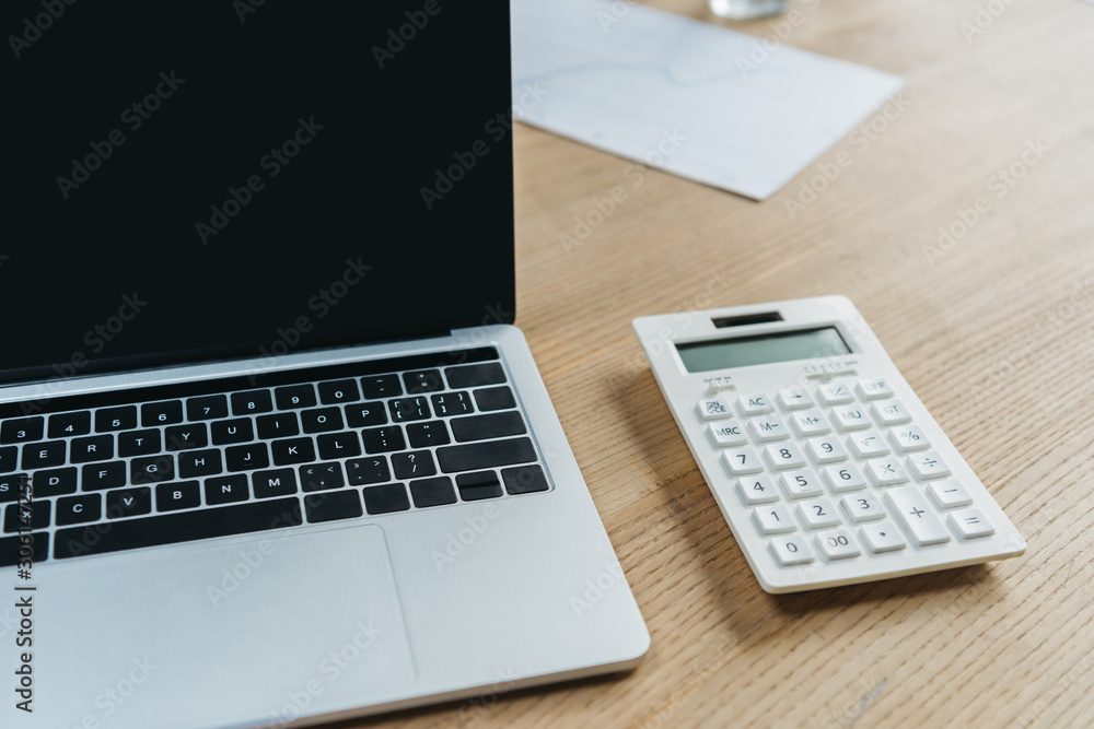 laptop with blank screen and calculator on wooden table laptop with blank screen and calculator on wooden table
