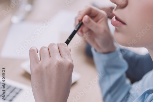 cropped view of young businesswoman holding pen during business meeting