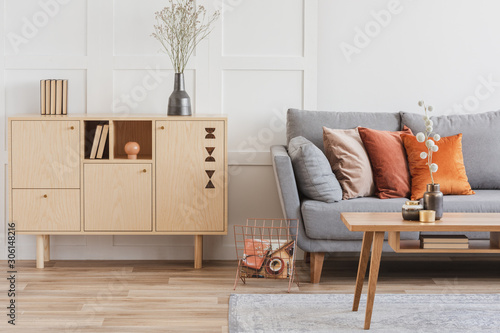 Wooden furniture and grey scandinavian sofa with pillows in beautiful living room interior photo