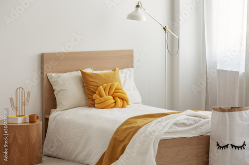 Foto Tall industrial lamp over yellow pillows and blanket on white single wooden bed