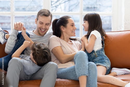 Happy parents playing with little kids relaxing on couch