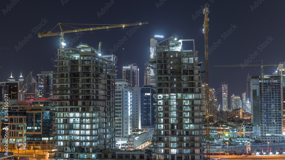 Obraz premium Aerial view of a skyscrapers under construction with huge cranes night timelapse in Dubai.