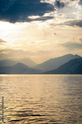 A sunset view of the Italian Alps over the calm waters of Lake Garda, Italy, at dusk.