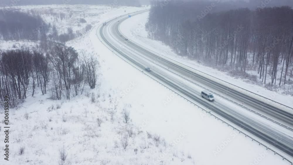 Aerial view of traffic on a road surrounded by winter forest in snowfall Aerial view of traffic on a road surrounded by winter forest in snowfall