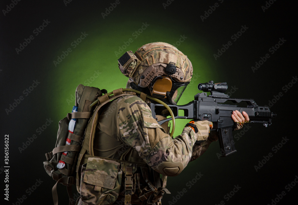 Fototapeta premium a male soldier in military clothes with a weapon on a dark background in a gas mask