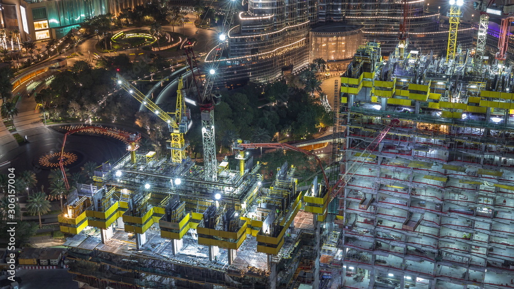 Aerial view of a skyscraper under construction with huge cranes night timelapse in Dubai.