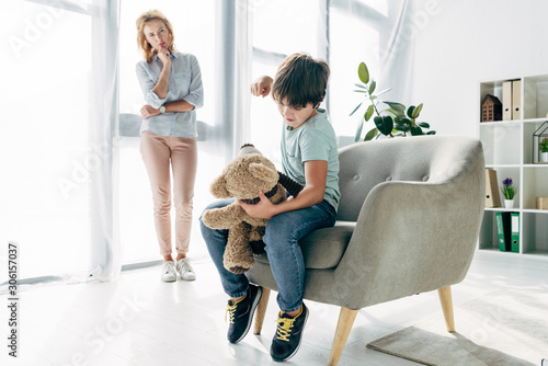 angry kid with dyslexia punching teddy bear and child psychologist looking at it photo