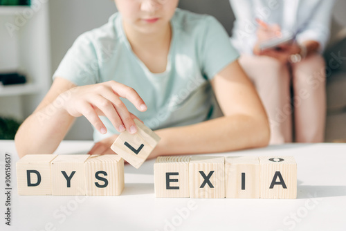 cropped view of kid with dyslexia sitting at table and playing with wooden cubes photo