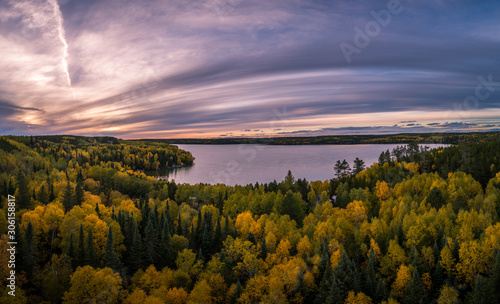 Fototapeta Naklejka Na Ścianę i Meble -  An aerial view of a forest in fall colors along a lake under an usual sunset sky.