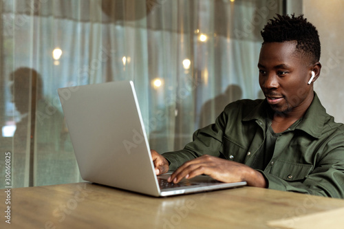 Cheerful young african american man in headphones using computer in cafe