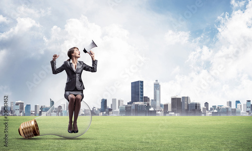 Woman with megaphone sitting on big light bulb