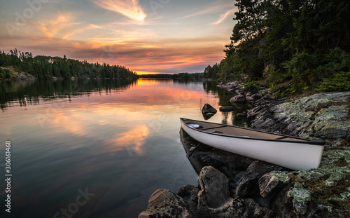 Fototapeta Naklejka Na Ścianę i Meble -  A lone canoe sits on shore on a peaceful lake at sunset. The odd colored clouds in the background are from a forest fire in Northwest Ontario, Canada in the summer of 2018.