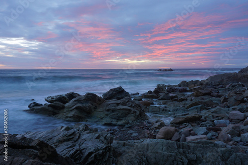 Motion-blurred waves crashing on a rocky shoreline under a red sunset © PT Hamilton