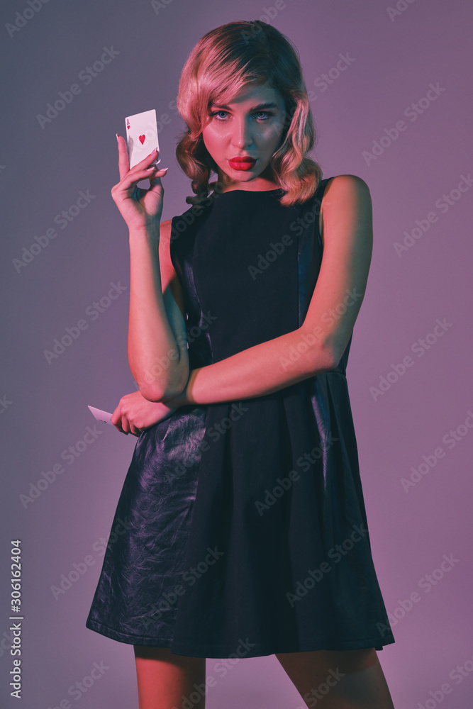Blonde girl in black stylish dress showing two playing cards, posing against colorful background. Gambling entertainment, poker, casino. Close-up. Blonde girl in black stylish dress showing two playing cards, posing against colorful background. Gambling entertainment, poker, casino. Close-up.