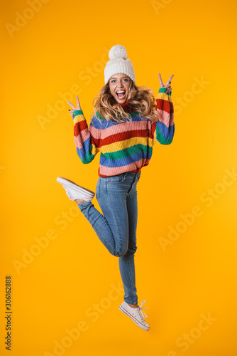 Full length image of blonde woman in winter hat showing peace fingers