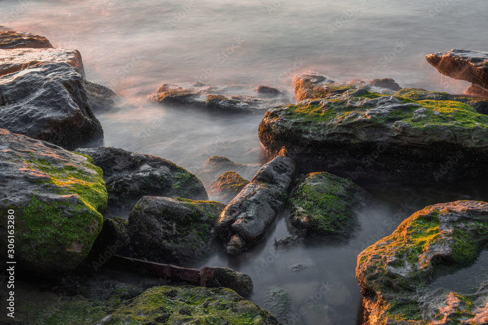 Fototapeta premium Rocky sea shore with blurred calm water