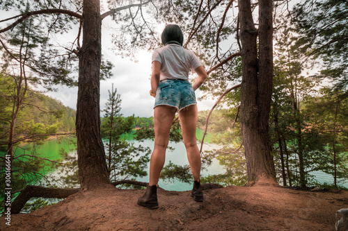 Fit girl standing near the lake, under a summer sky and sun rays. View from behind