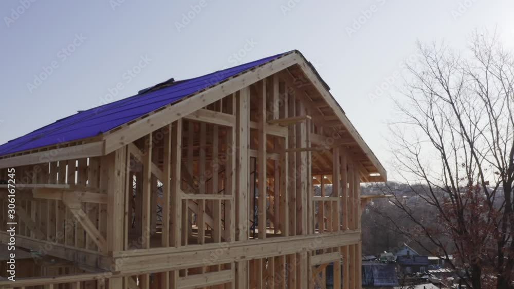 Zooming out aerial view of wooden frame house under construction in sunny autumn day. Roof is covered with insulation material, the roof base Zooming out aerial view of wooden frame house under construction in sunny autumn day. Roof is covered with insulation material, the roof base