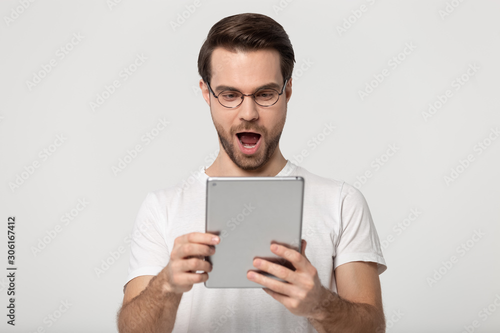 Excited Caucasian guy in glasses feel shocked using tablet Excited Caucasian guy in glasses feel shocked using tablet