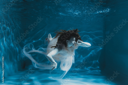A girl with long dark hair swims underwater in a pink dress and with a crown on her head, like an underwater queen. Fairy tale suitable for advertising