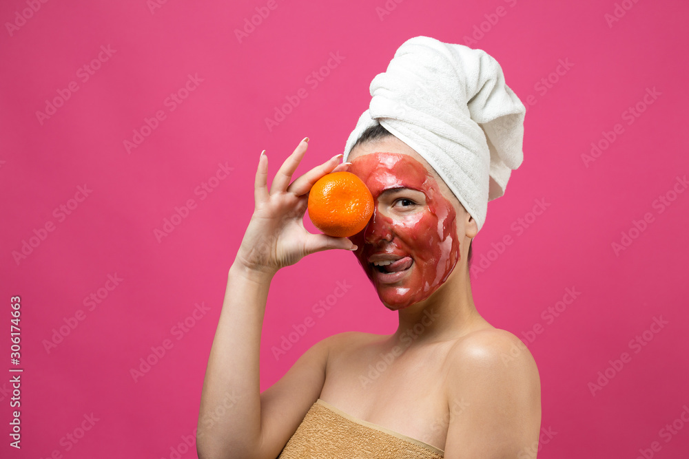 Beauty portrait of woman in white towel on head with red nourishing mask on face. Skincare cleansing eco organic cosmetic spa relax concept. A girl stands with her back holding an orange mandarin. Beauty portrait of woman in white towel on head with red nourishing mask on face. Skincare cleansing eco organic cosmetic spa relax concept. A girl stands with her back holding an orange mandarin.