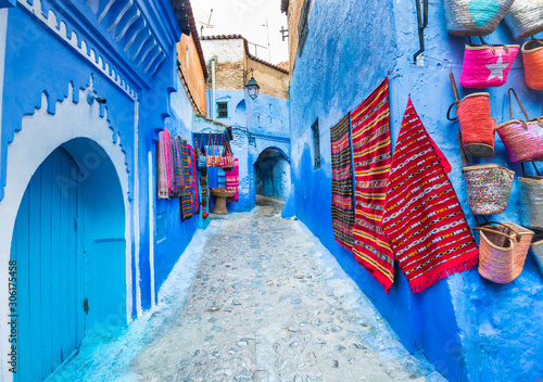 Blue street of Chefchaouen in Morocco with colorful carpets and handicrafts on walls © leelook