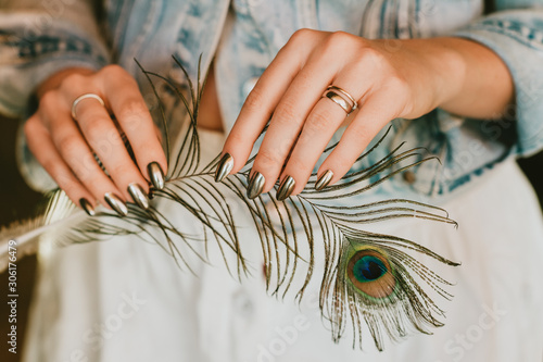 Bild auf Leinwand Stylish trendy female mirror manicure, metal nail art, holding peacock feather