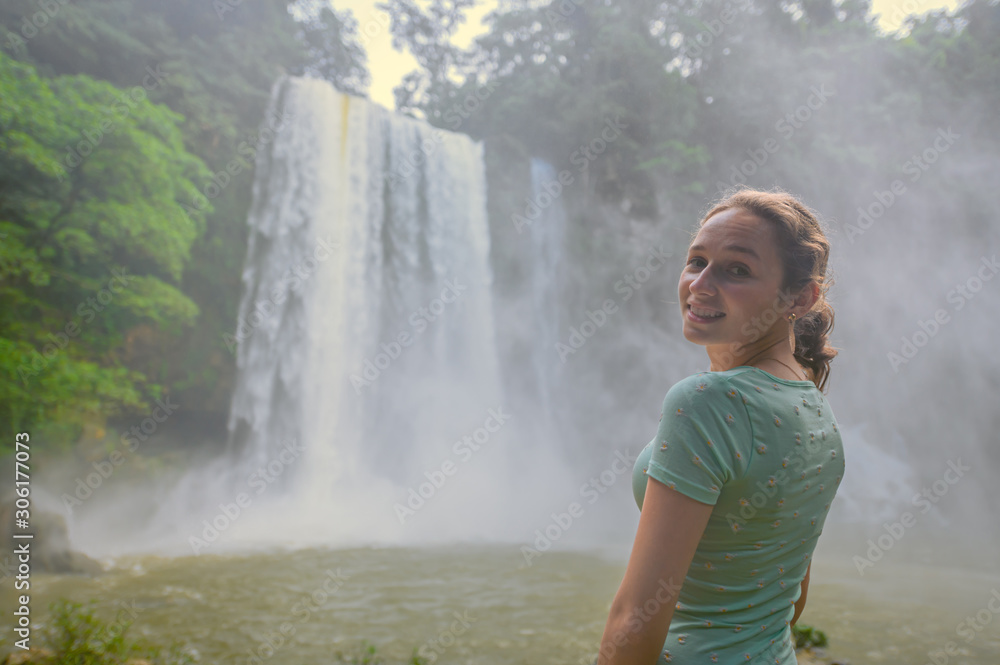 Young blond woman standing on a rock watching the landscape with a waterfall in the middle of the jungle Young blond woman standing on a rock watching the landscape with a waterfall in the middle of the jungle