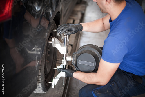 Wheel alignment. Car mechanic installing sensor during suspension adjustment