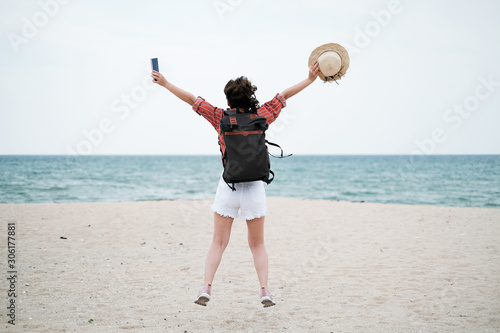 Happy young woman is relaxing and jumping with bag pack on sandy beach and seaside background, Holiday planing and traveling concept